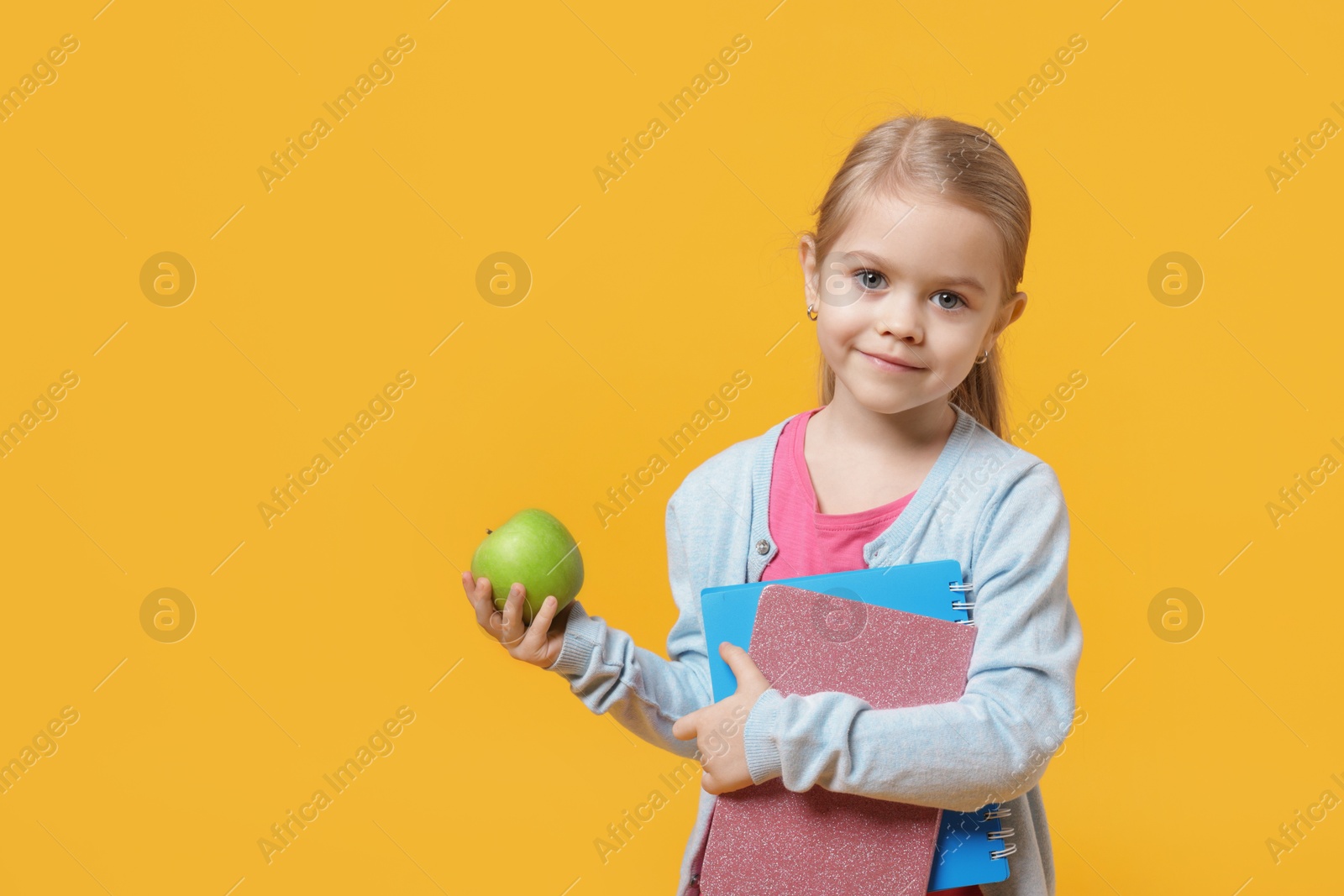 Photo of Cute little girl with books and apple on orange background. Space for text