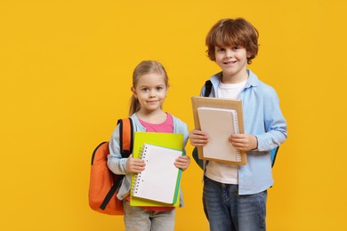 Cute little children with backpacks and books on orange background