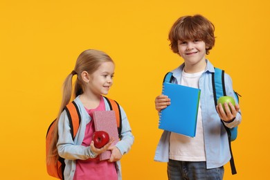 School children with books and apples on orange background