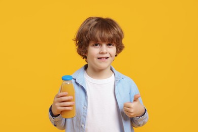 Photo of Little boy with drink showing thumbs up on orange background