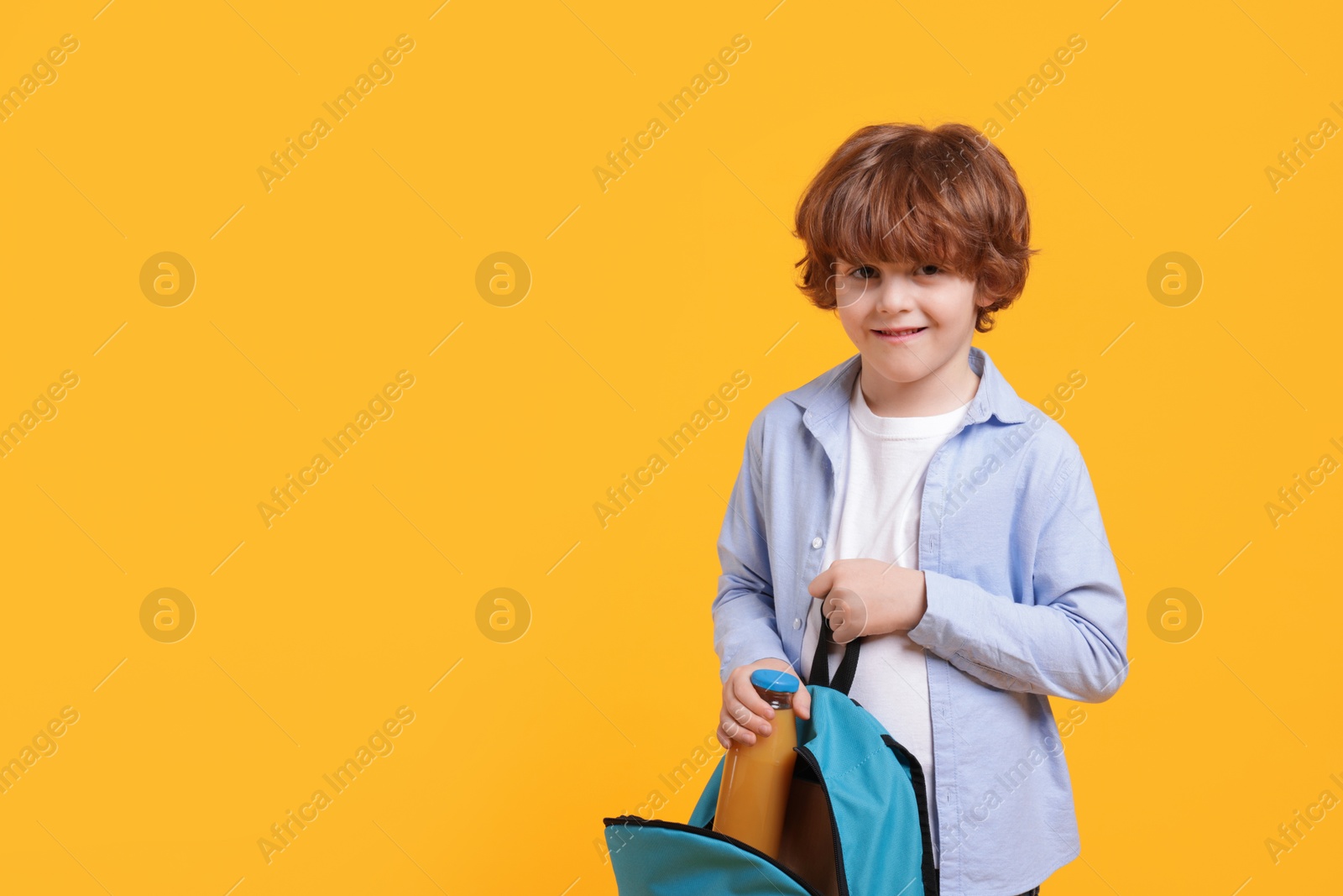 Photo of Little boy packing drink into backpack on orange background. Space for text