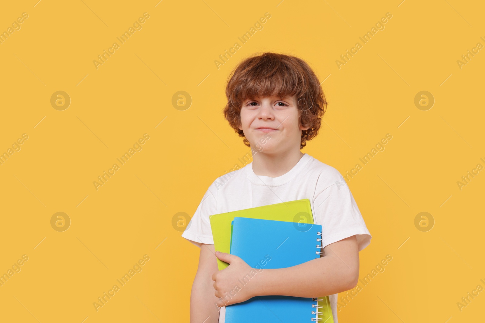 Photo of Cute little boy with books on orange background. Space for text