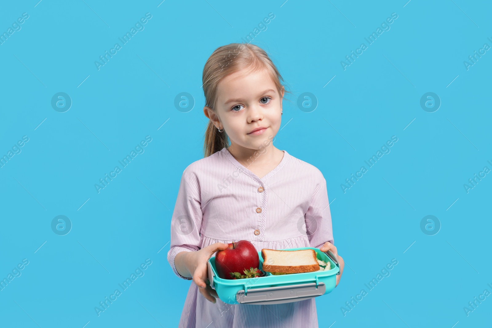 Photo of Cute little girl with lunch box on light blue background