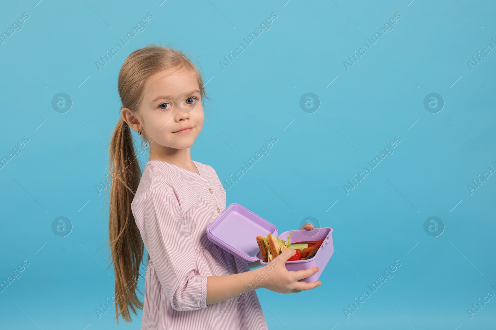 Photo of Cute little girl with lunch box on light blue background. Space for text