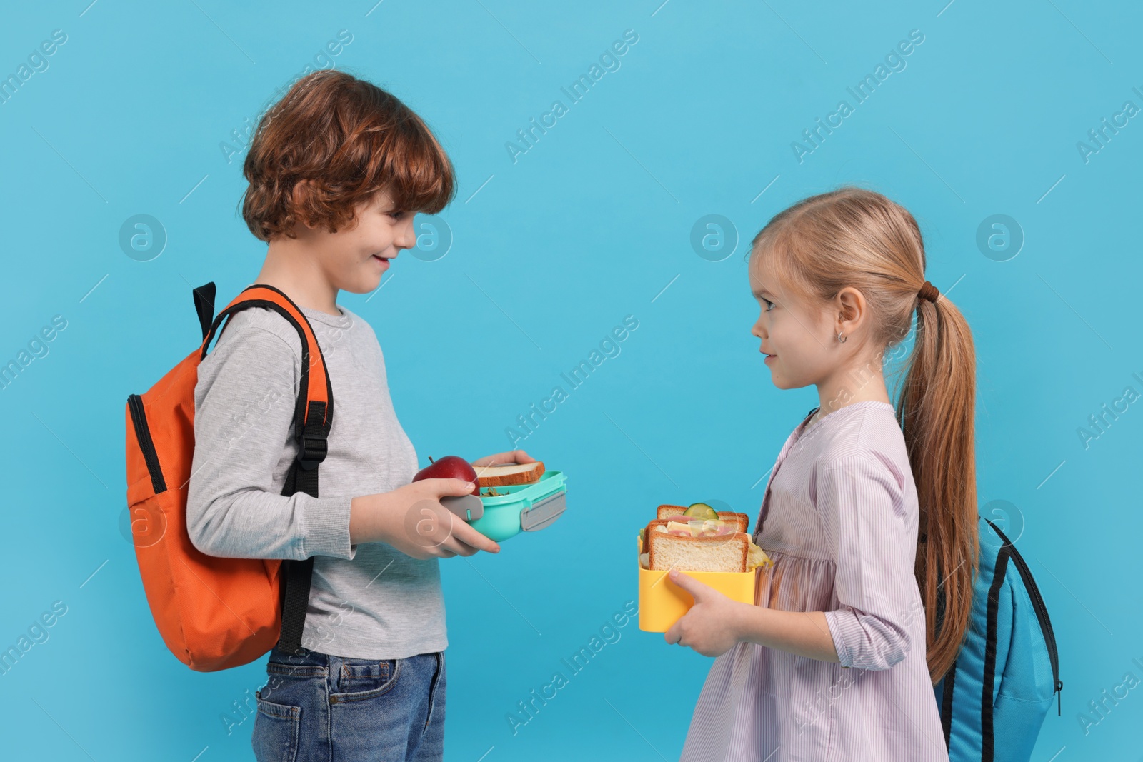 Photo of Cute little children with lunch boxes on light blue background