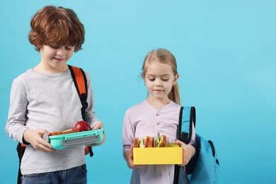 Cute little children with lunch boxes on light blue background