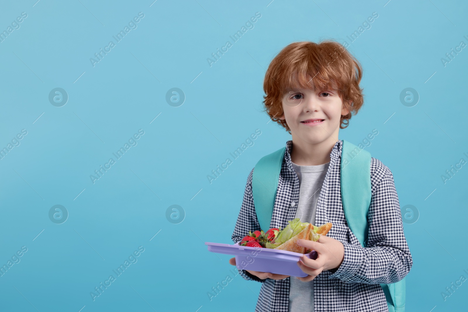 Photo of Cute little boy with lunch box on light blue background. Space for text