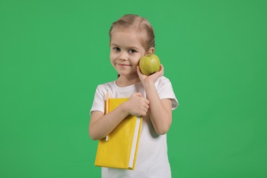 Photo of Cute little girl with book and apple on green background