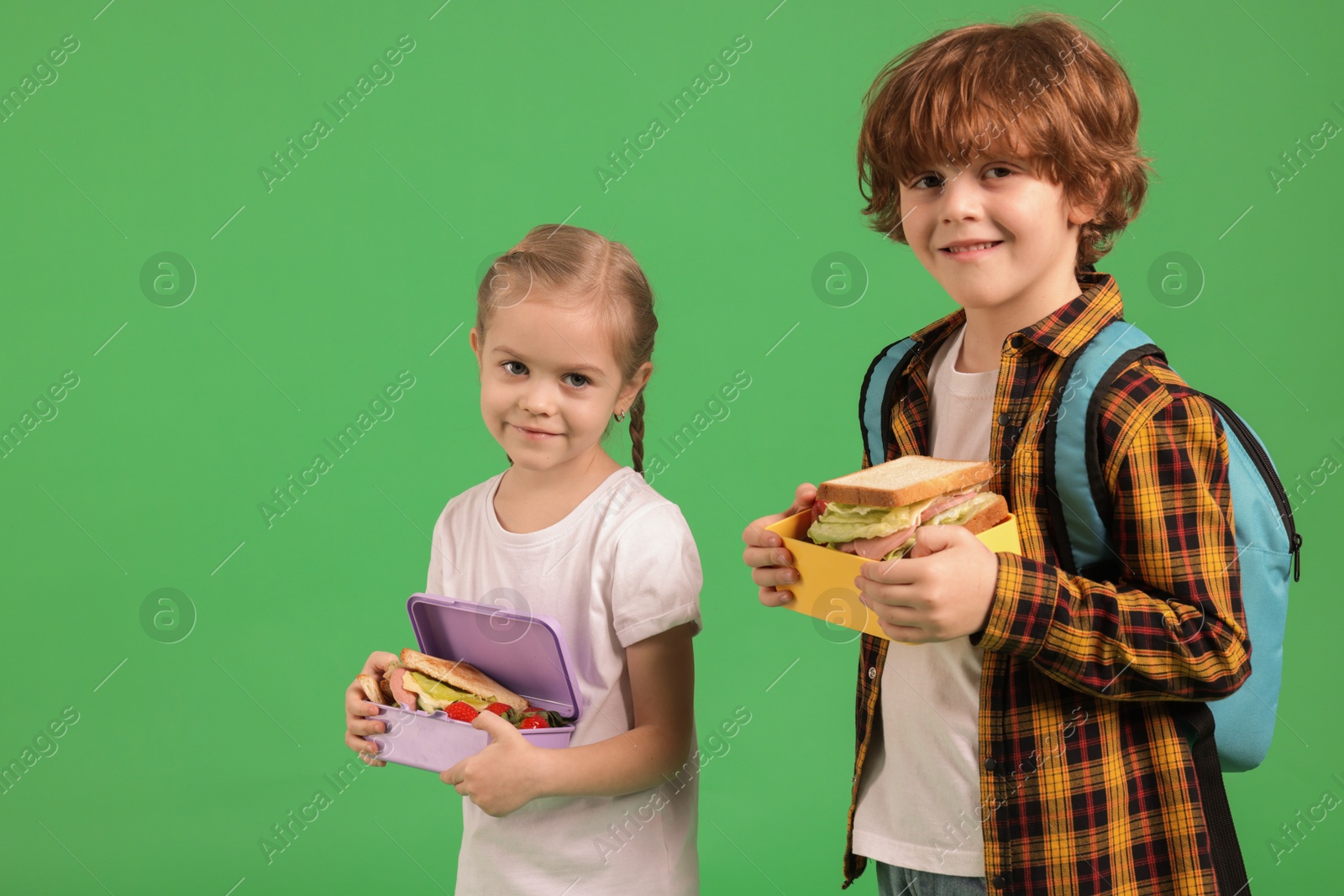 Photo of Cute little children with lunch boxes on green background. Space for text