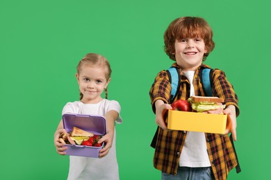 Cute little children with lunch boxes on green background