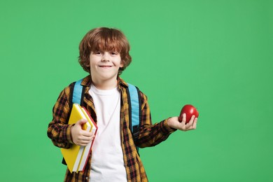 Photo of Cute little boy with books and apple on green background. Space for text