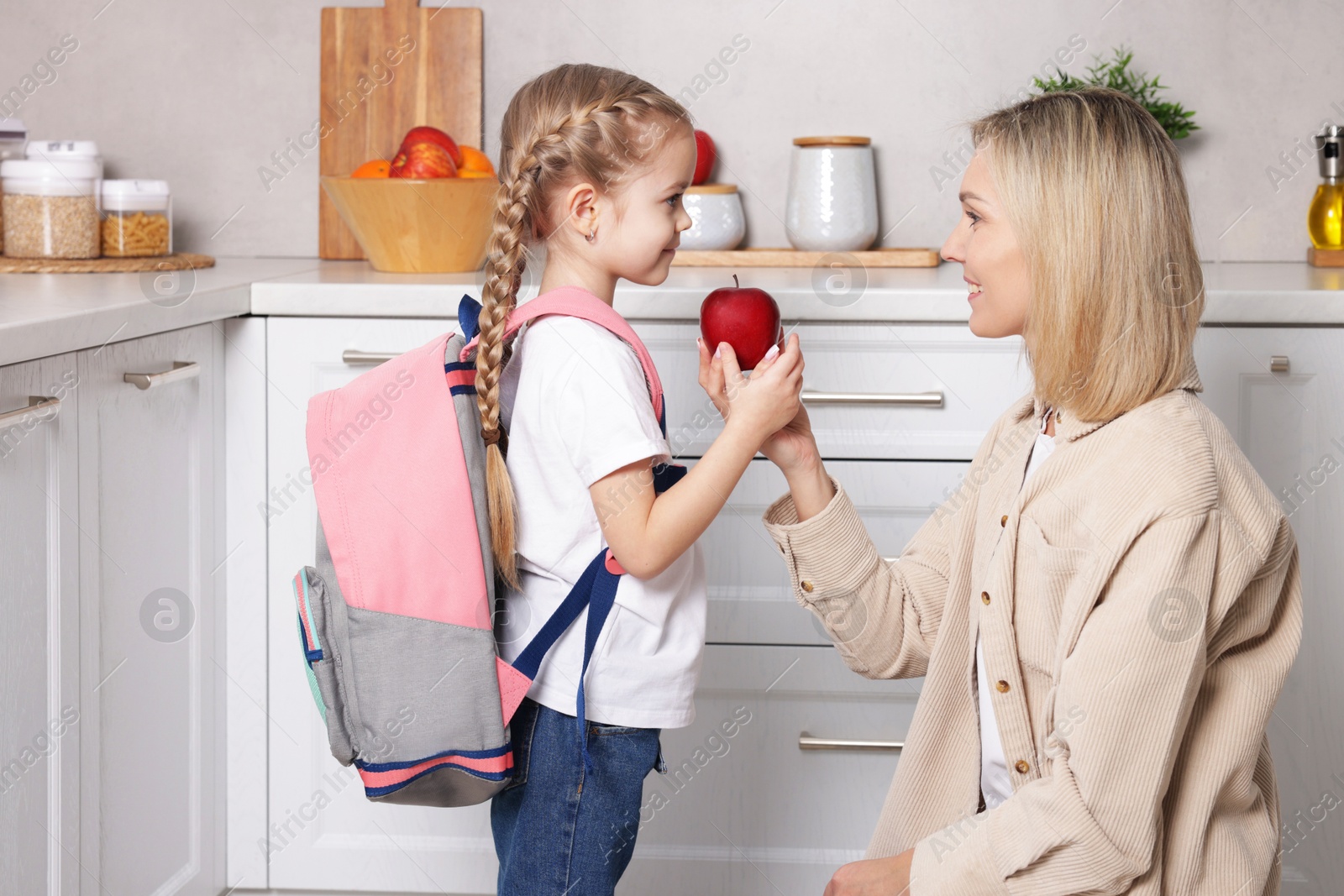 Photo of Mother giving her daughter apple for school snack in kitchen