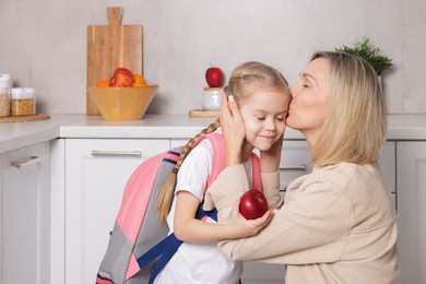 Mother giving her daughter apple for school snack in kitchen. Space for text