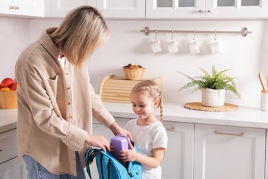 Mother packing her daughter's lunch in kitchen. Space for text