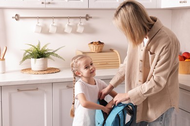 Photo of Mother and daughter packing backpack for school at home