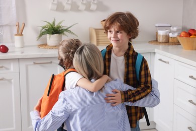 Photo of Mother and her cute children with backpacks hugging at home