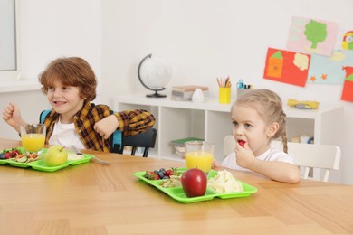 Cute little children eating lunch at wooden table in school