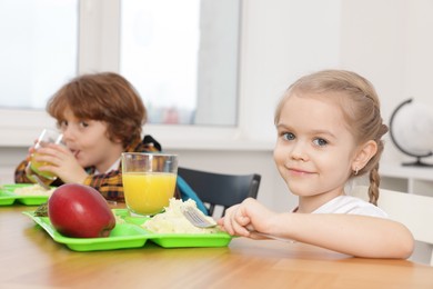 Photo of Cute little children eating lunch at wooden table in school