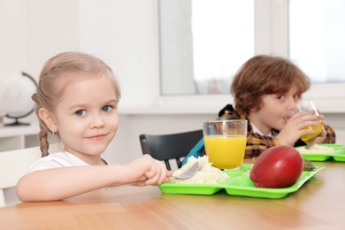 Photo of Cute little children eating lunch at wooden table in school