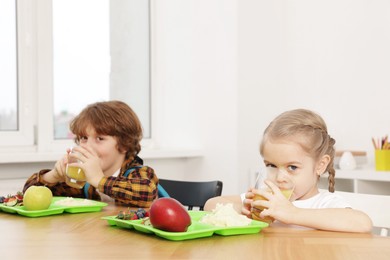 Photo of Cute little children eating lunch at wooden table in school