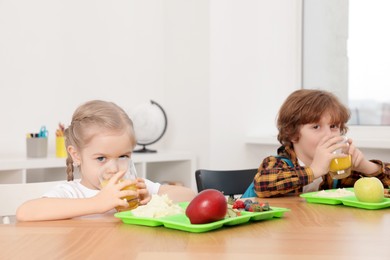 Photo of Cute little children eating lunch at wooden table in school