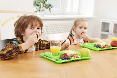 Photo of Cute little children eating lunch at wooden table in school