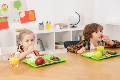 Photo of Cute little children eating lunch at wooden table in school