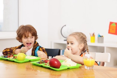 Photo of Cute little children eating lunch at wooden table in school