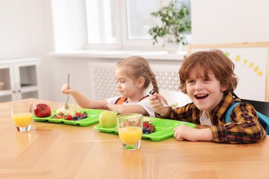 Photo of Cute little children eating lunch at wooden table in school