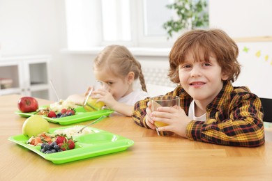 Photo of Cute little children eating lunch at wooden table in school