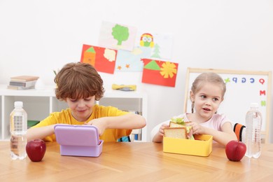 Photo of Cute little children eating lunch at wooden table in school