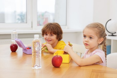 Photo of Cute little children eating lunch at wooden table in school