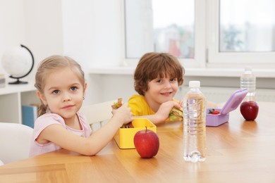 Photo of Cute little children eating lunch at wooden table in school