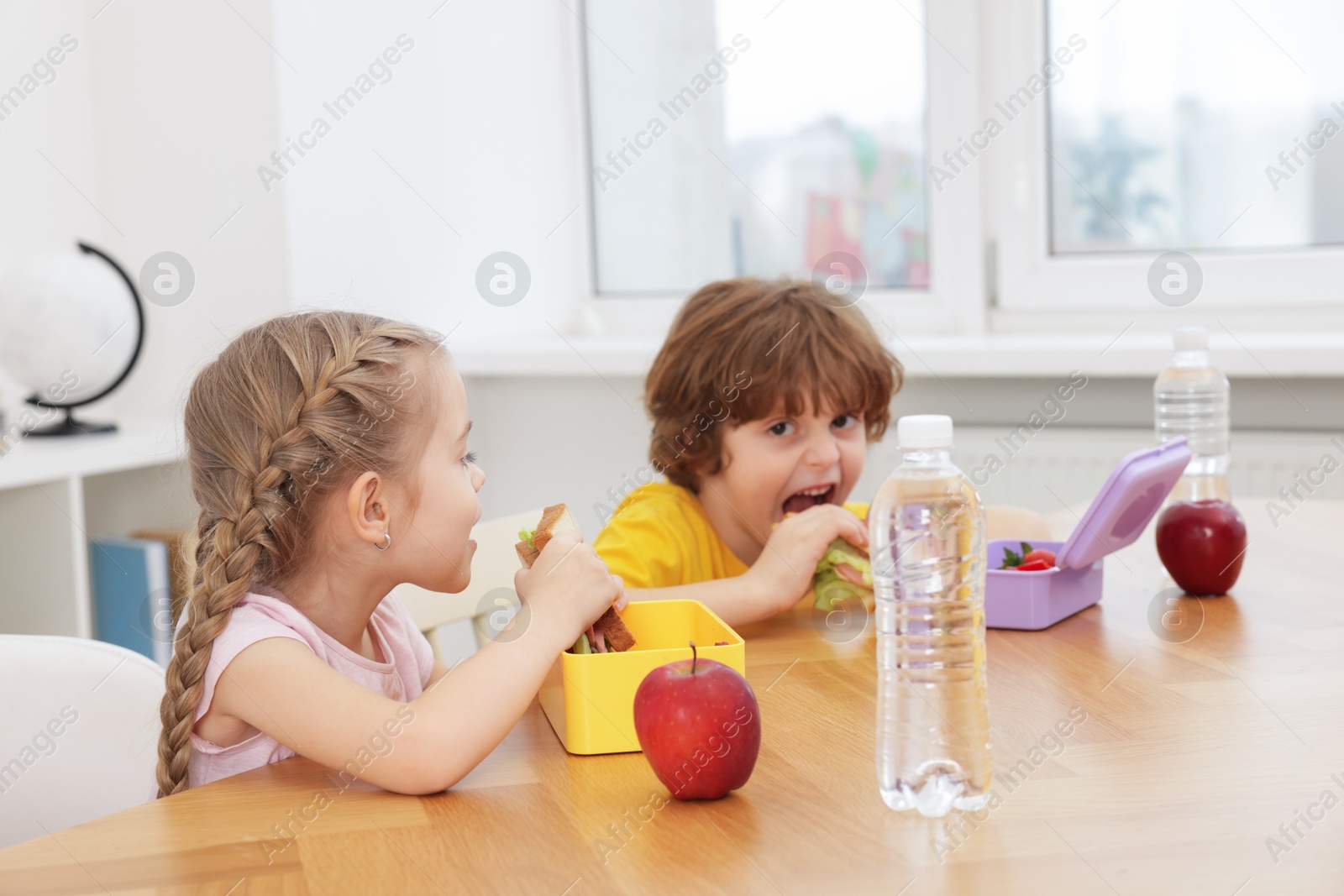 Photo of Cute little children eating lunch at wooden table in school