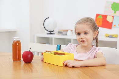 Photo of Cute little girl eating lunch at wooden table in school. Space for text