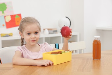 Photo of Cute little girl eating lunch at wooden table in school