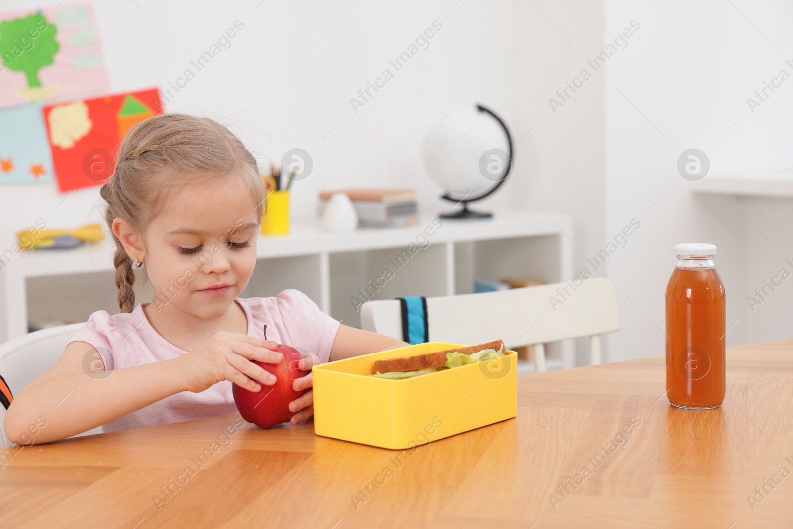 Photo of Cute little girl eating lunch at wooden table in school. Space for text