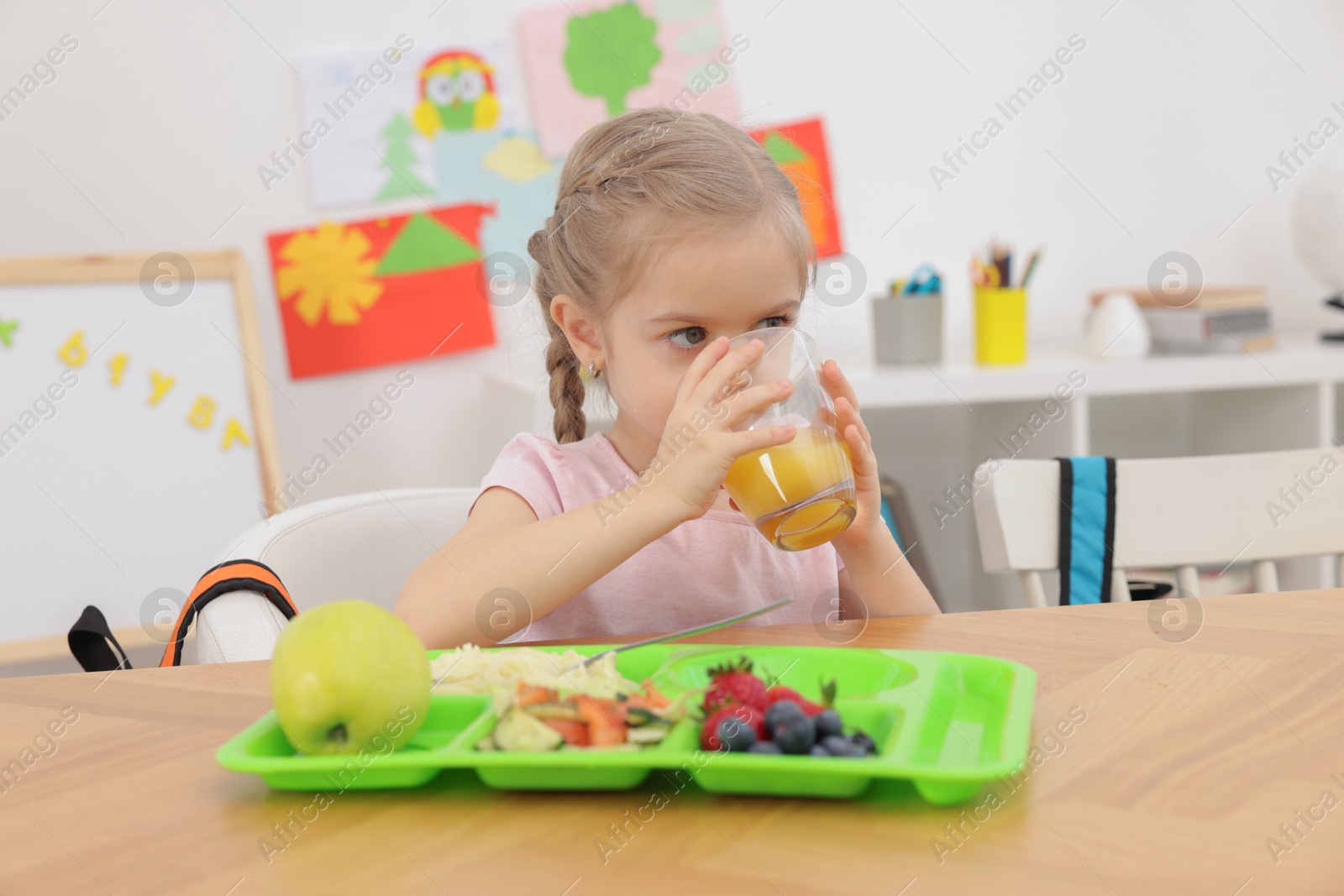 Photo of Cute little girl eating lunch at wooden table in school