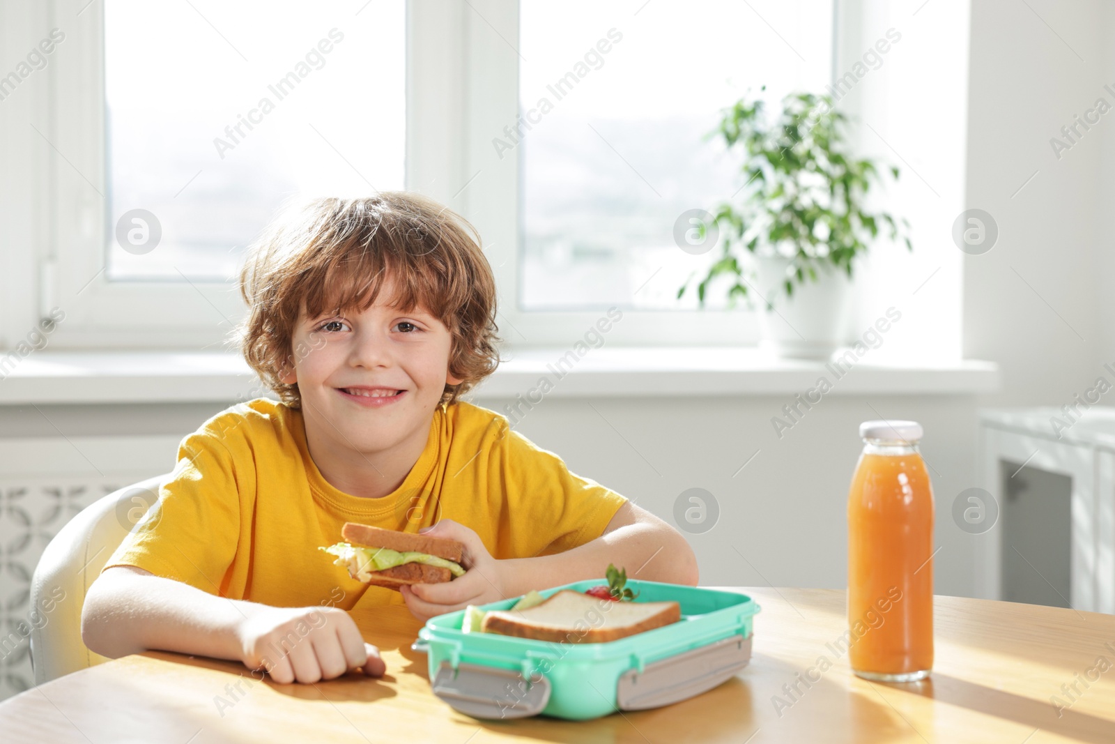 Photo of Cute little boy eating lunch at wooden table in school. Space for text