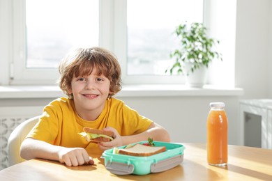 Photo of Cute little boy eating lunch at wooden table in school. Space for text