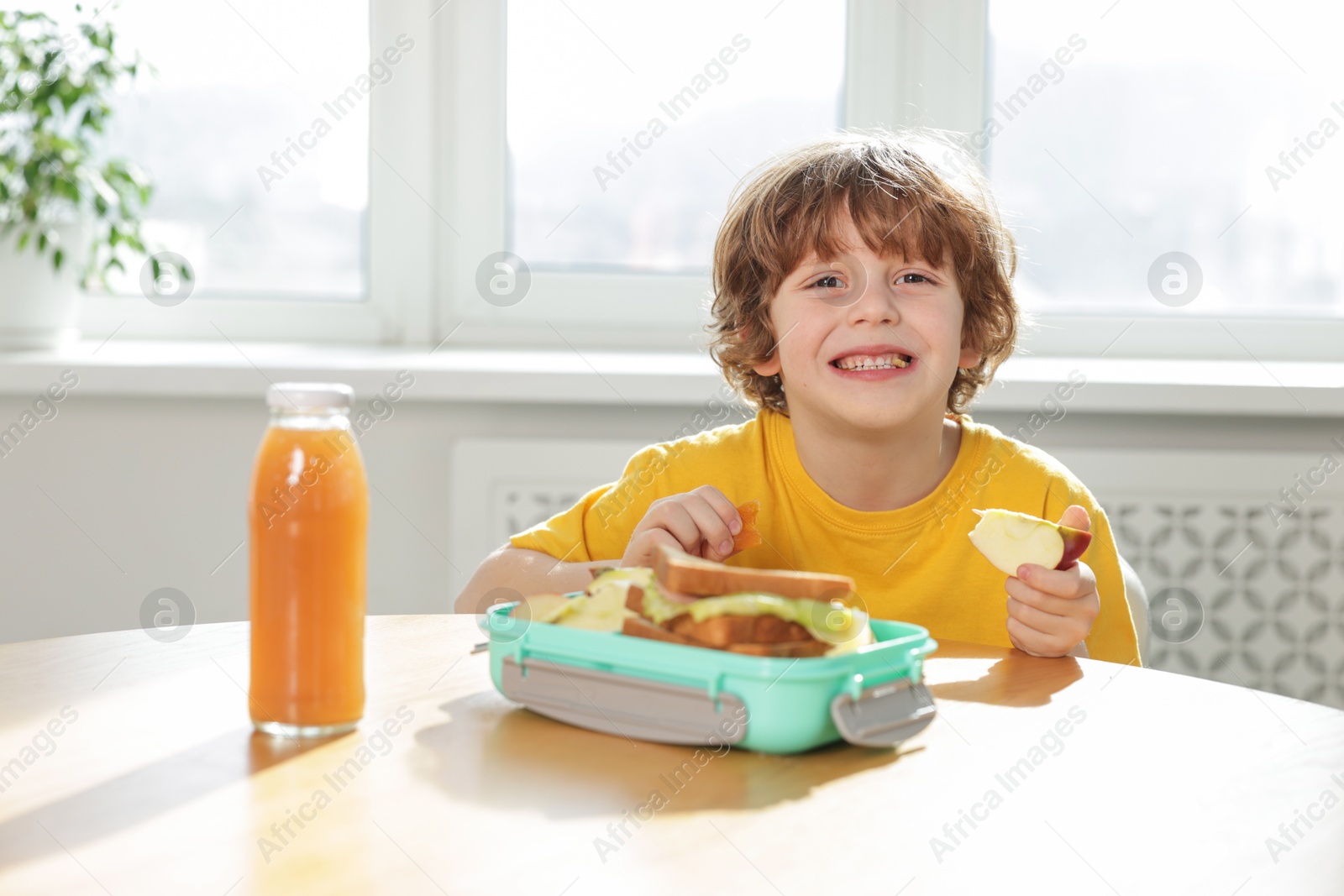 Photo of Cute little boy eating lunch at wooden table in school