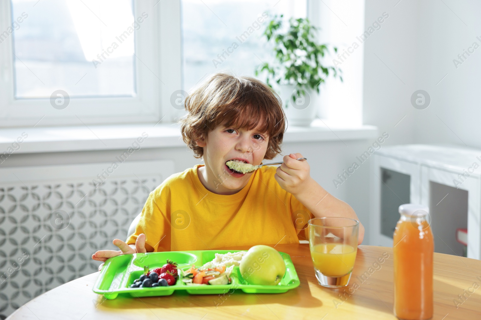 Photo of Cute little boy eating lunch at wooden table in school