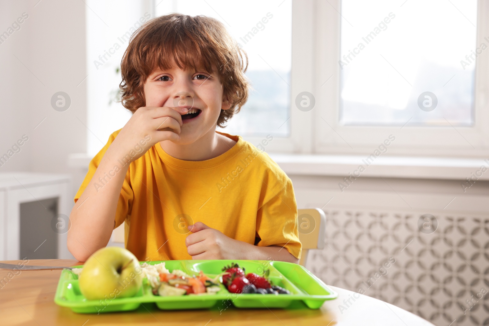 Photo of Cute little boy eating lunch at wooden table in school. Space for text