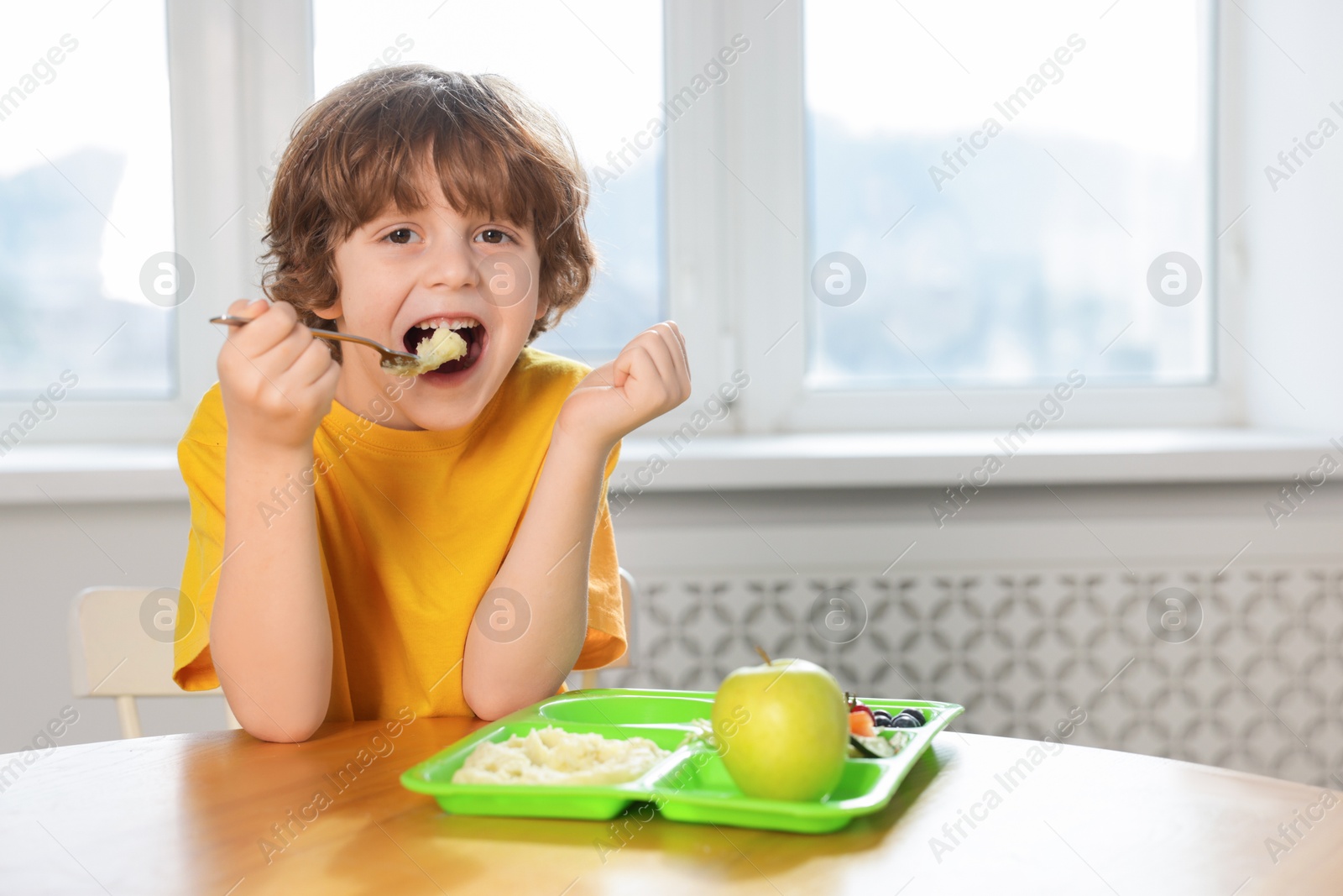 Photo of Cute little boy eating lunch at wooden table in school. Space for text