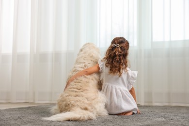 Photo of Little girl with cute dog on carpet at home, back view