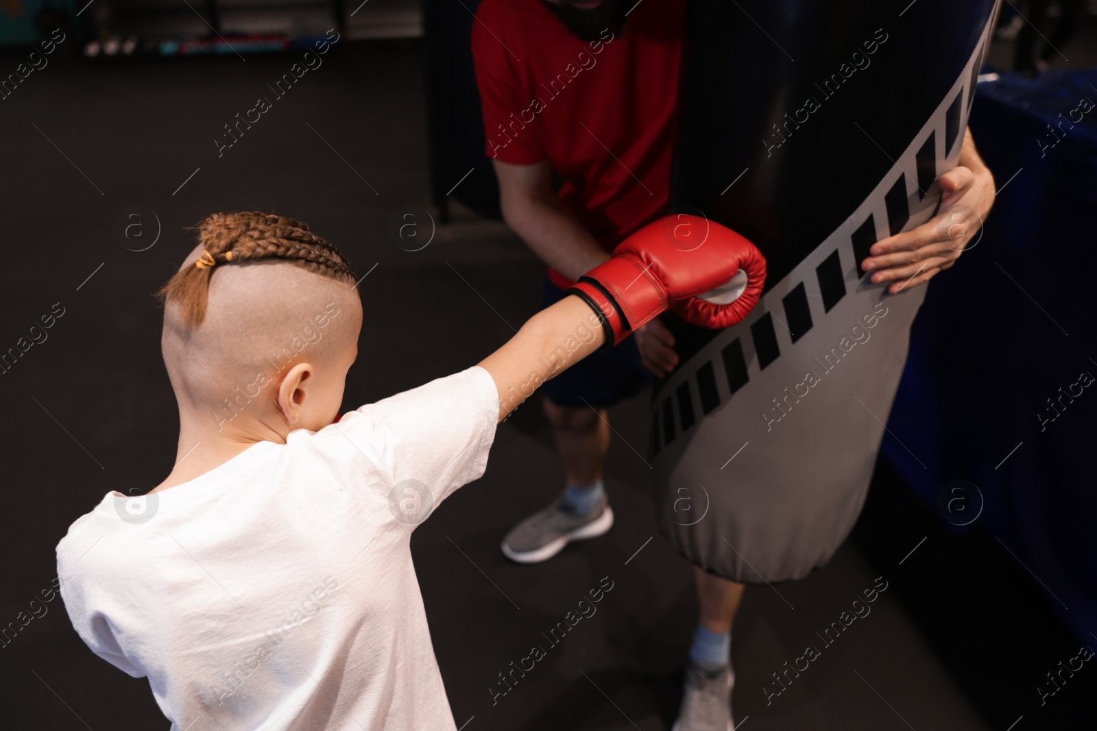 Photo of Boy in protective gloves with his boxing coach at training center