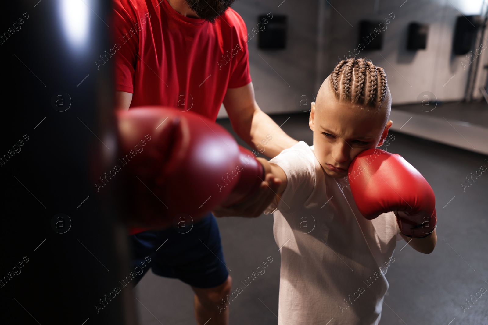 Photo of Boy in protective gloves with his boxing coach at training center