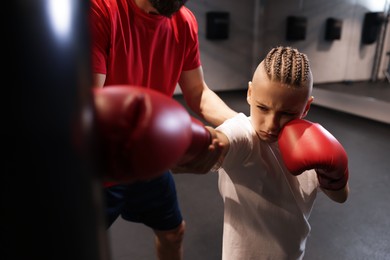 Photo of Boy in protective gloves with his boxing coach at training center