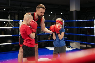 Photo of Children practicing fight on boxing ring under their coach supervision