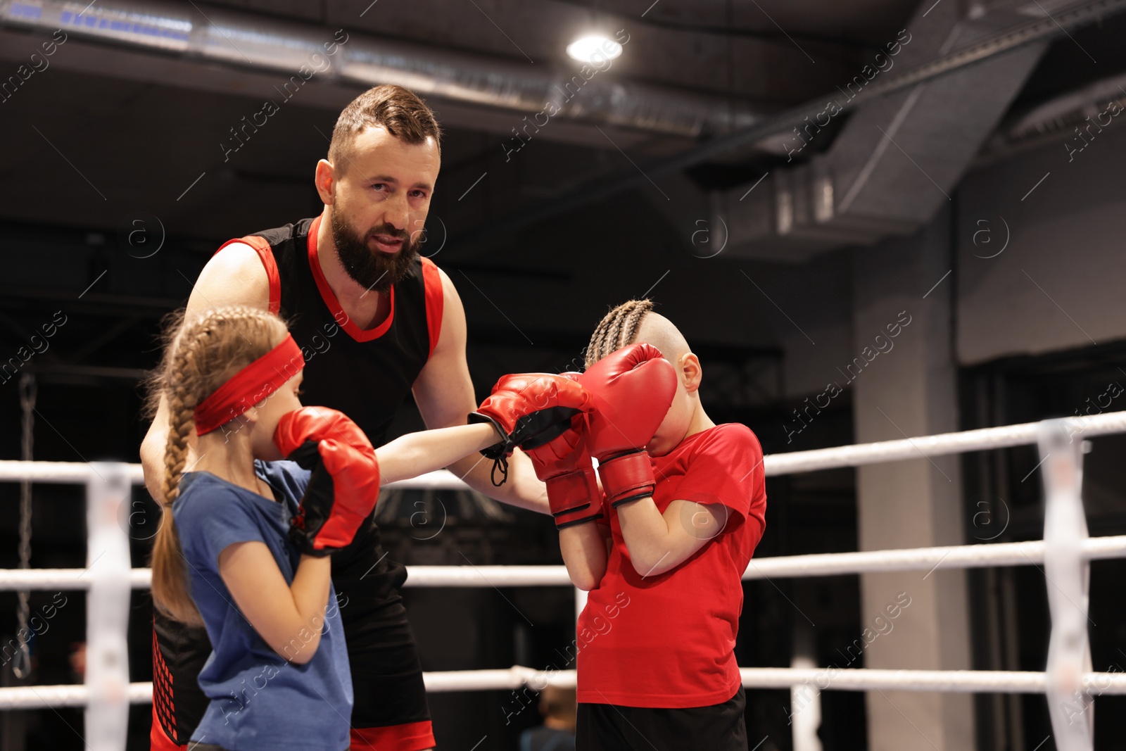 Photo of Children practicing fight on boxing ring under their coach supervision